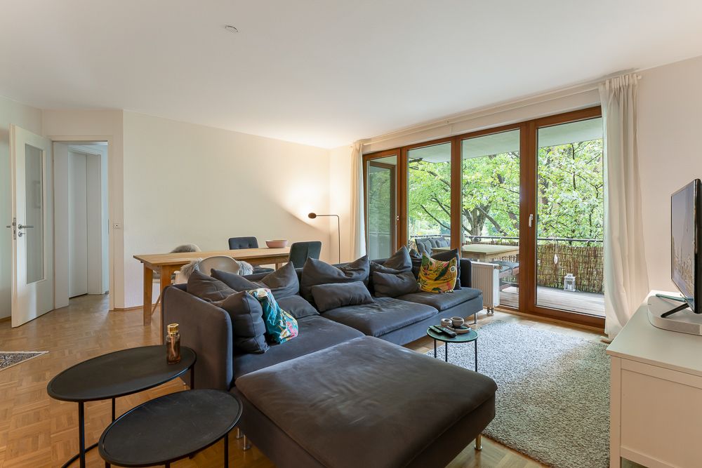 Helles Wohnzimmer mit Sofa, Couchtisch, Teppich, Esstisch und großen Fenstern zur Terrasse.