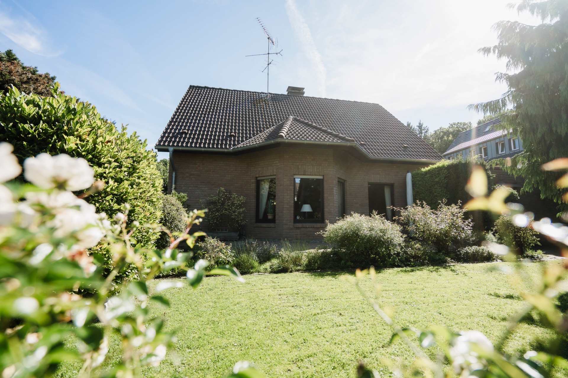 Backsteinhaus mit dunklem Dach und großem Garten im Vordergrund.