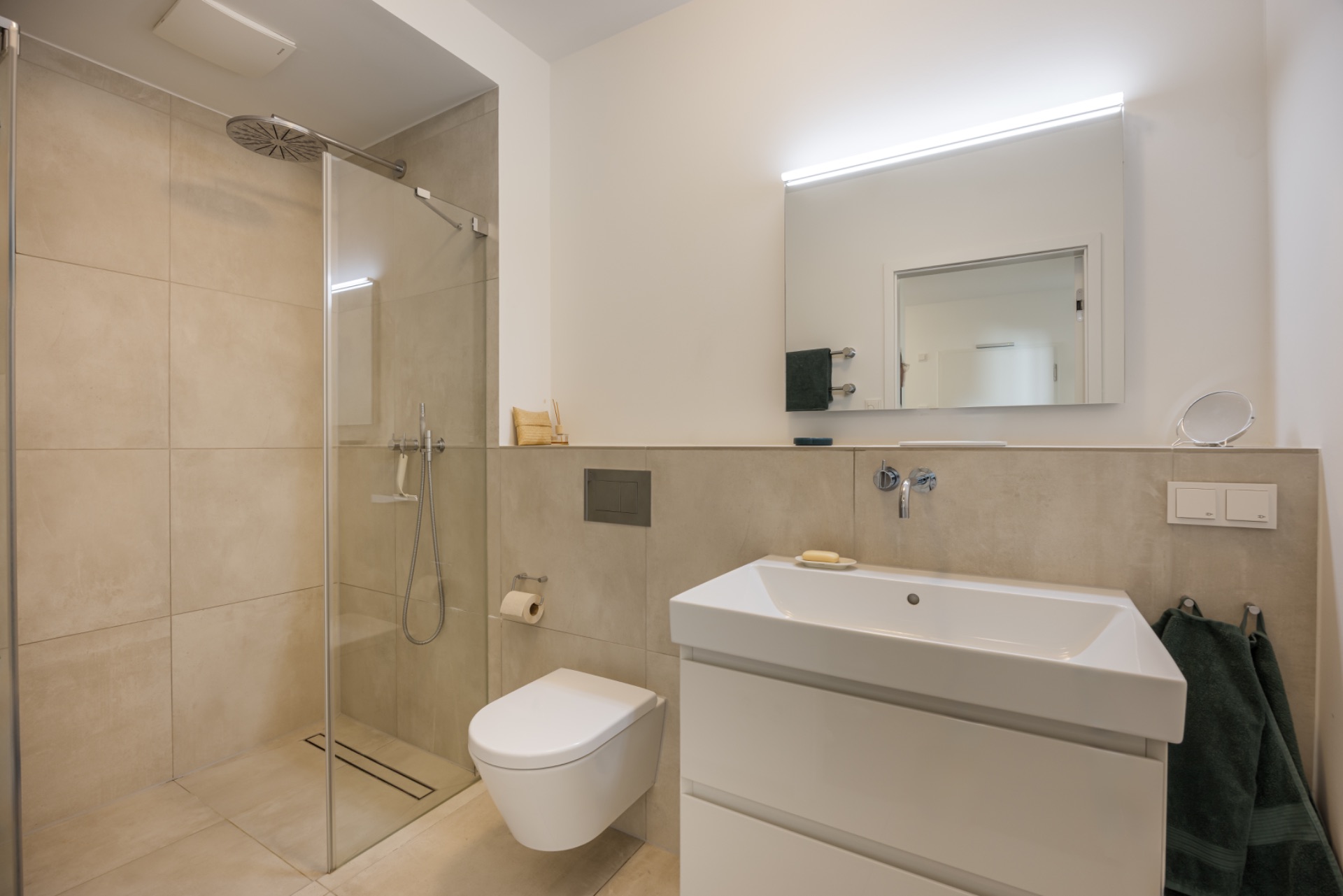 Modernes Bad mit ebenerdiger Dusche, Wandtoilette und Waschbecken mit Spiegel.