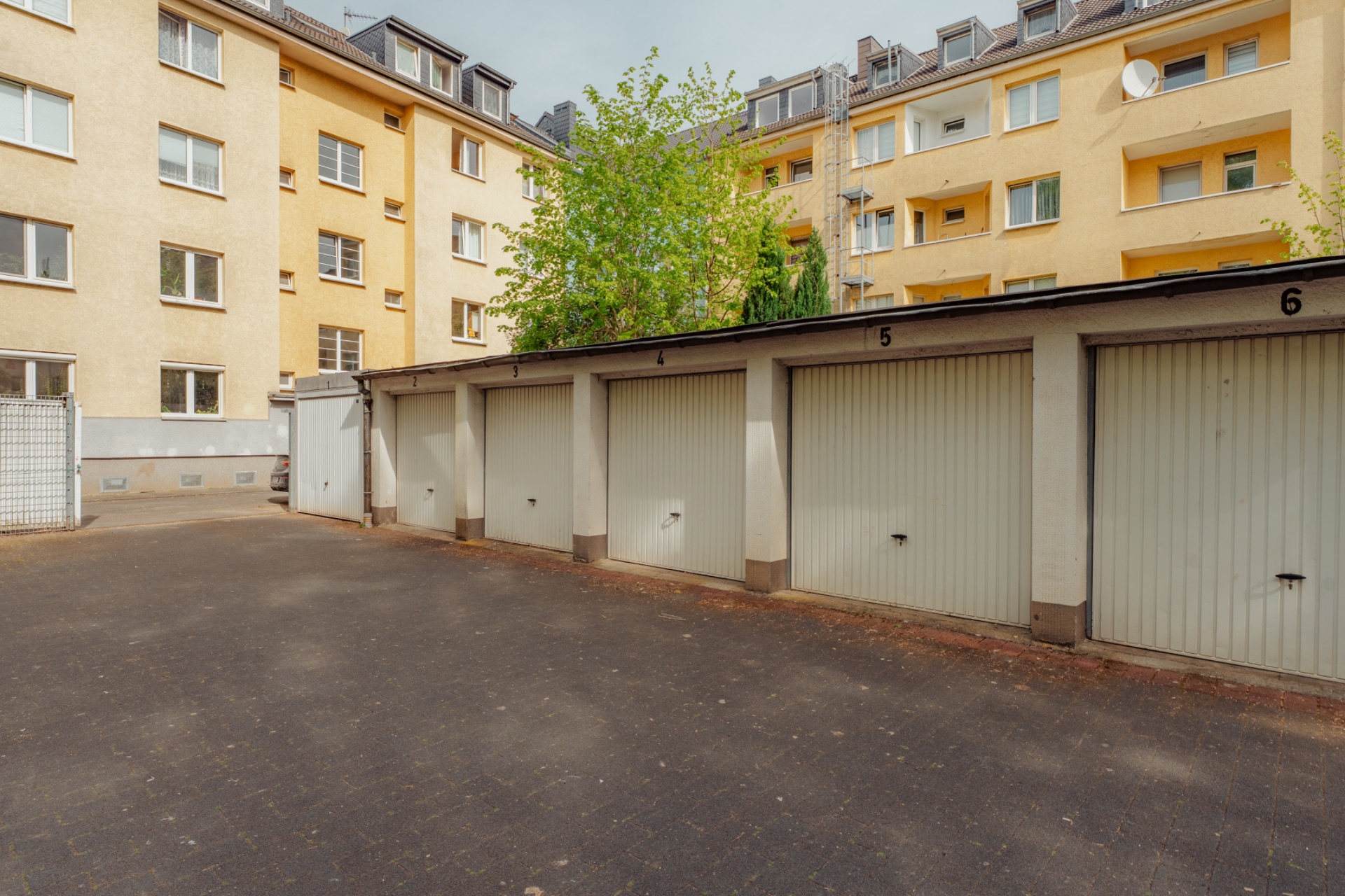 Reihe von Garagen mit nummerierten Toren vor einem Wohnhaus.