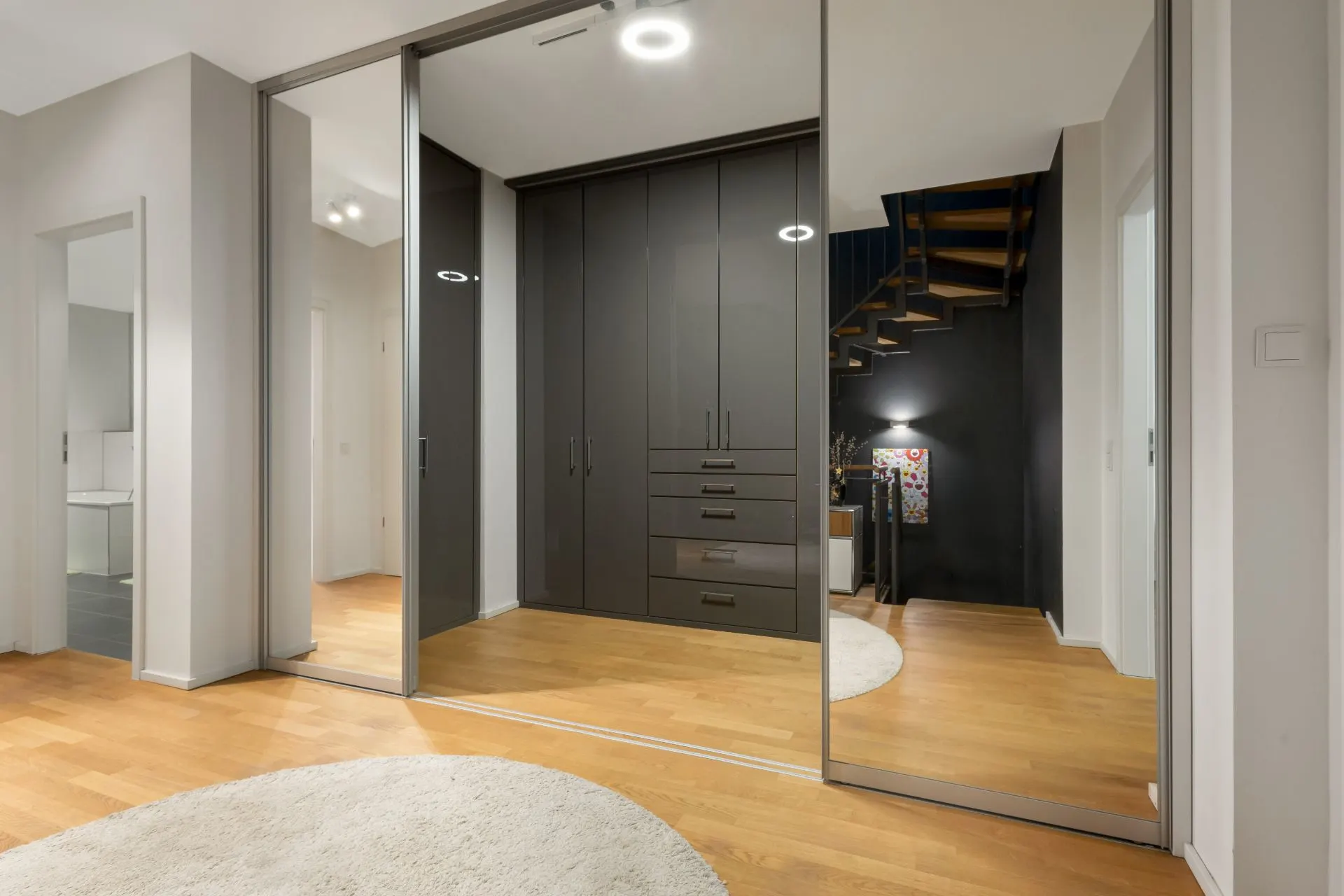 Flur mit Spiegelwänden, Holzfußboden, dunklem Einbauschrank und Treppe.