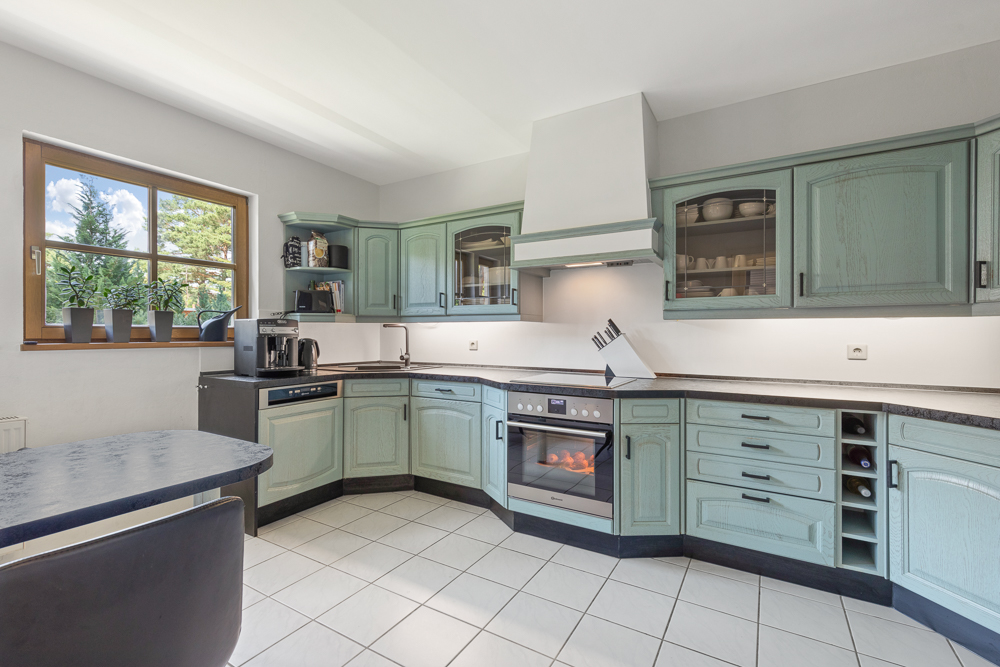 Helle Küche mit grünen Schränken, Elektroherd, Fenster und Esstisch.