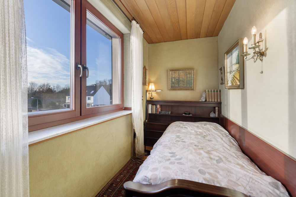 Kleines Schlafzimmer mit Einzelbett, großem Fenster, Wandlampen und Bücherregal.
