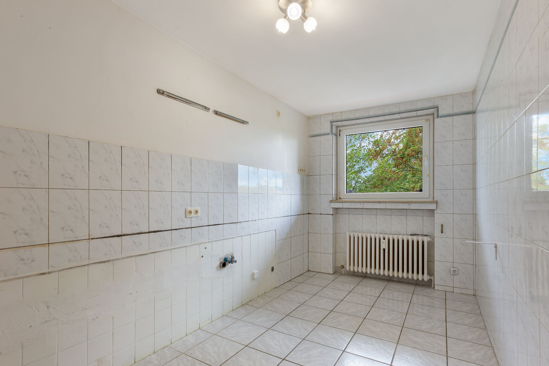 Leerer gefliester Raum mit Fenster, Heizung und Deckenleuchte.