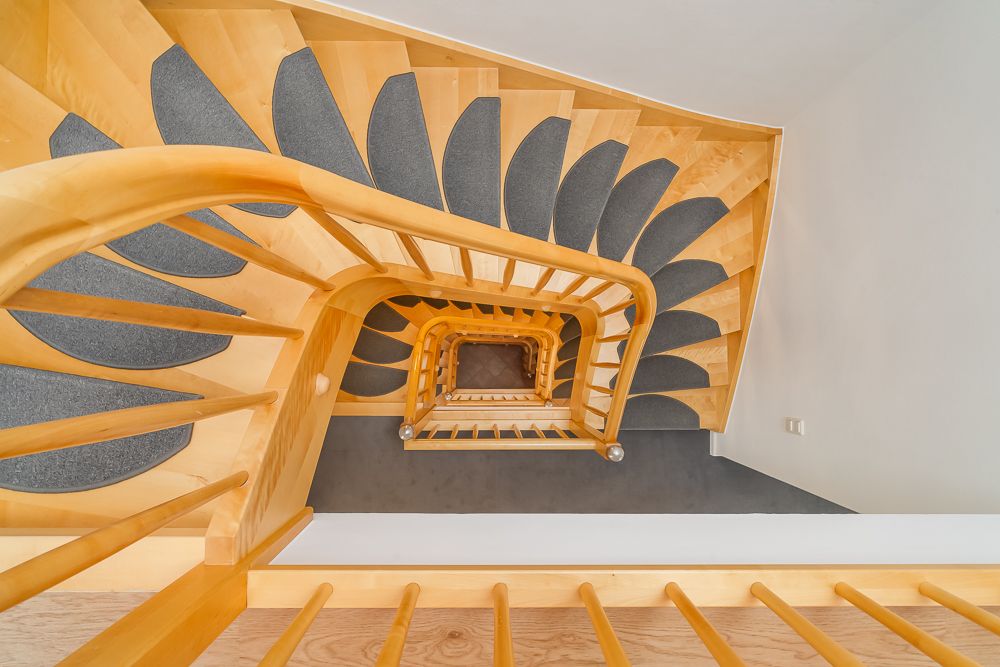 Blick von oben auf ein helles Holztreppenhaus mit grauen Stufenmatten in einem Wohnhaus.