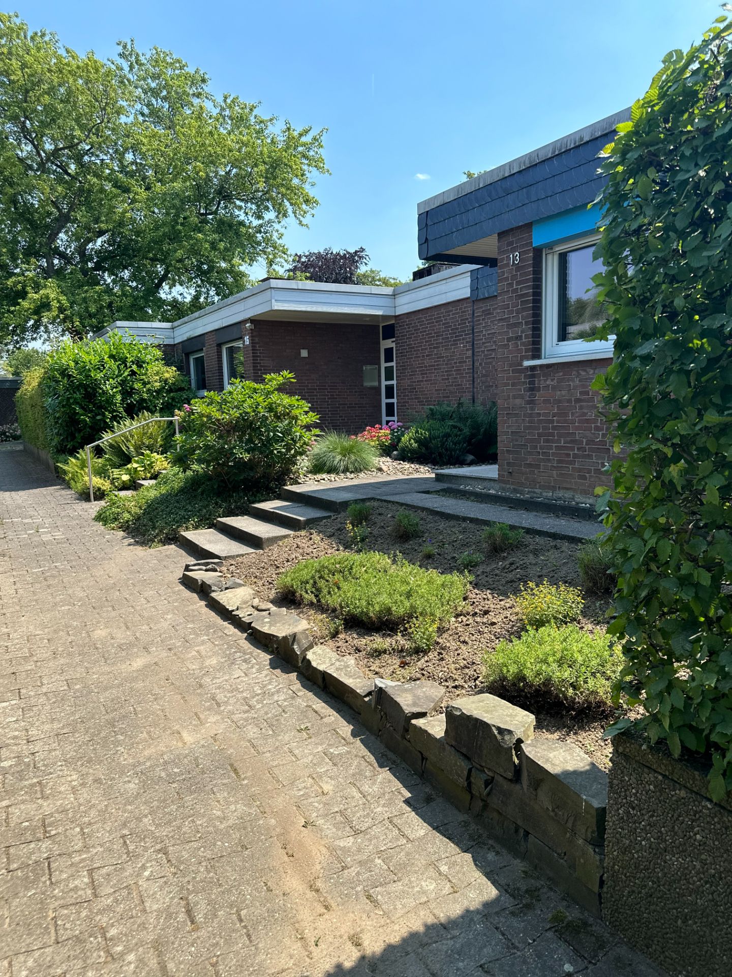 Eingangsbereich eines Backsteinhauses mit Garten, Gehweg und Stufen.
