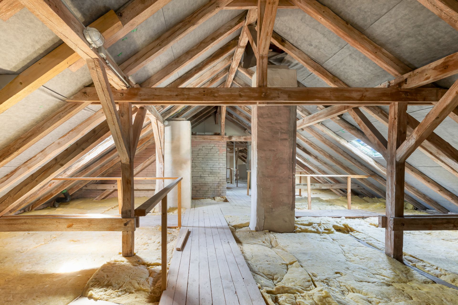 Dachboden mit sichtbaren Holzbalken, Dämmung und einem Holzsteg in der Mitte.