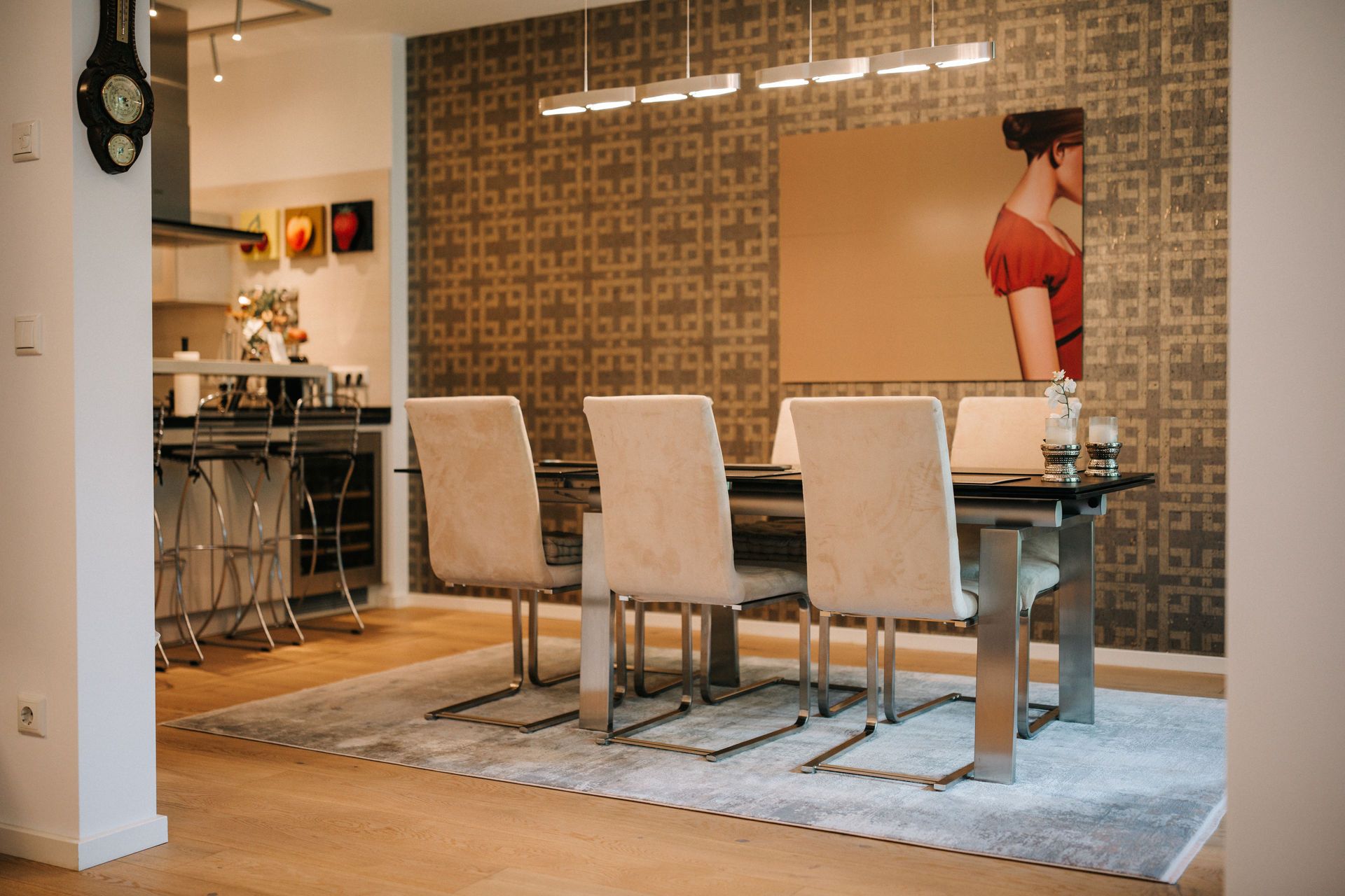 Esszimmer mit sechs Stühlen, Glastisch, Teppich und modernem Wandbild, angrenzende offene Küche.