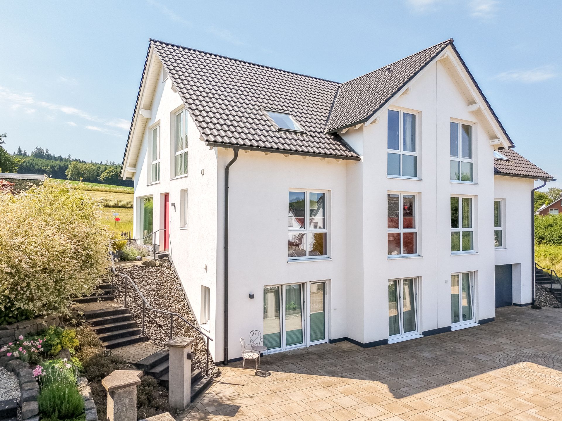 Modernes, weißes Wohnhaus mit großen Fenstern, Terrasse und Treppe im Garten.