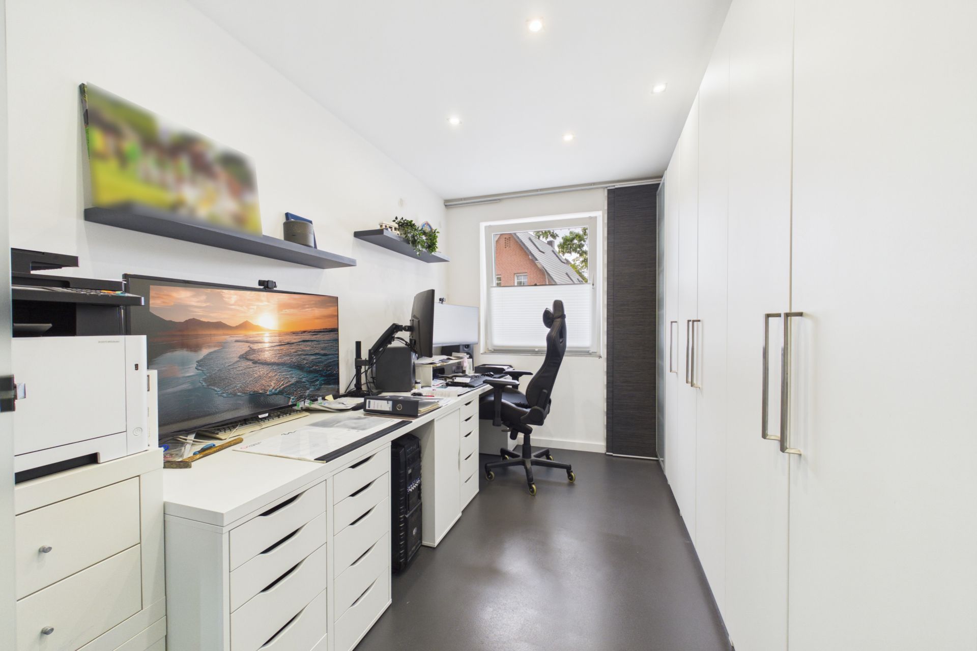 Modernes Arbeitszimmer mit Schreibtisch, Monitoren, Bürostuhl und weißen Schränken.