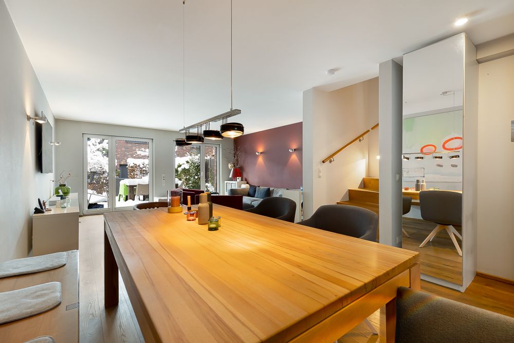 Esszimmer mit Holztisch und Stühlen, Blick auf Wohnzimmer, Treppe und Glastür zum Garten.