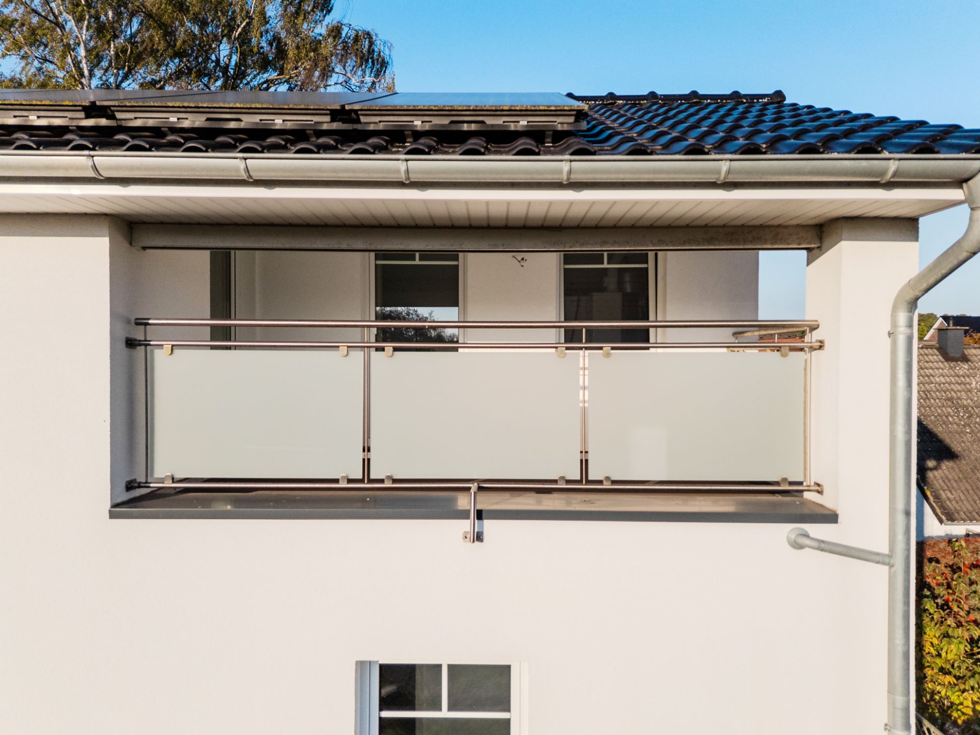Balkon mit milchglasähnlichem Geländer an einem modernen weißen Wohnhaus.