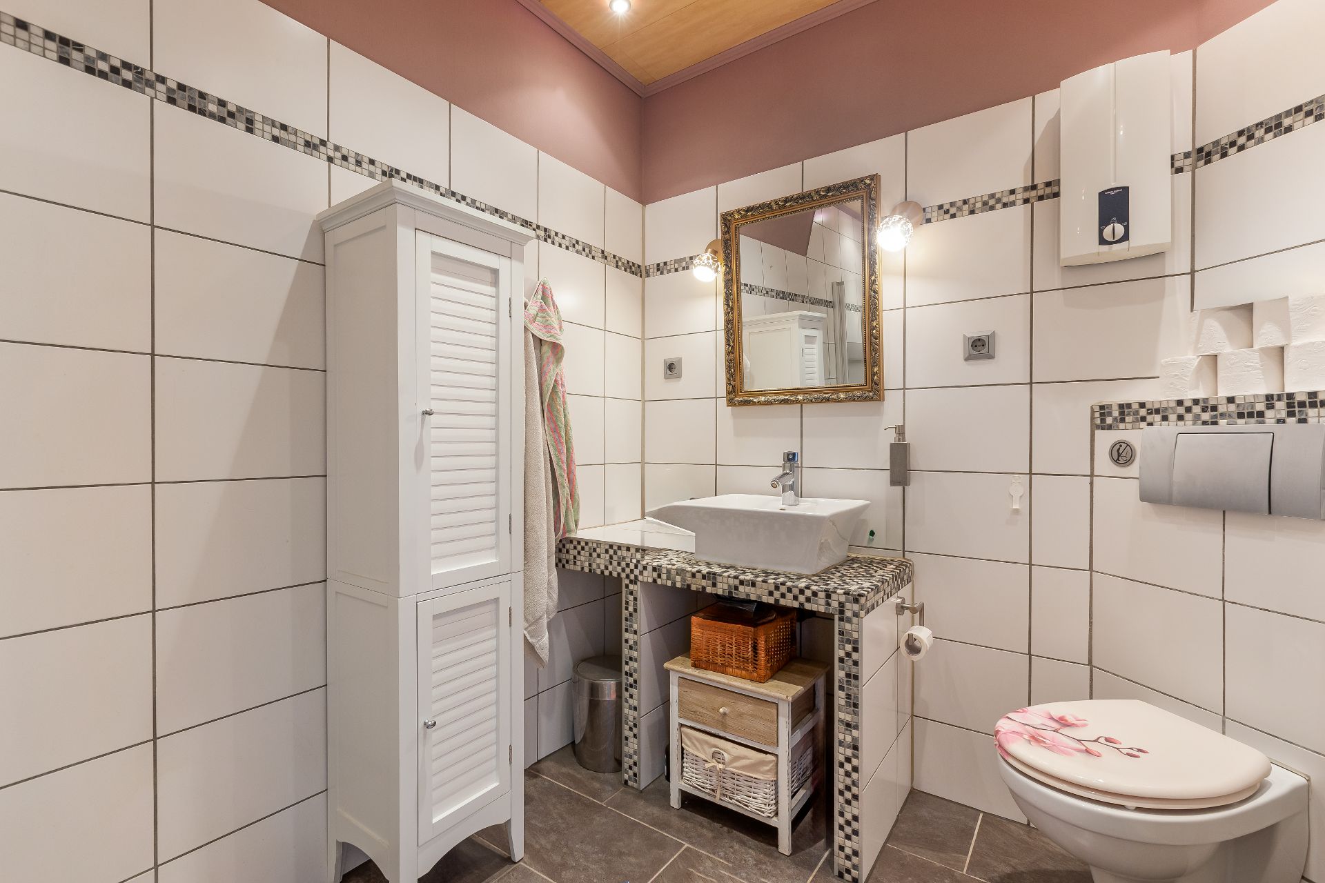 Modernes Badezimmer mit weißem Schrank, Waschbecken, Spiegel und Toilette mit Blumenmotiv.