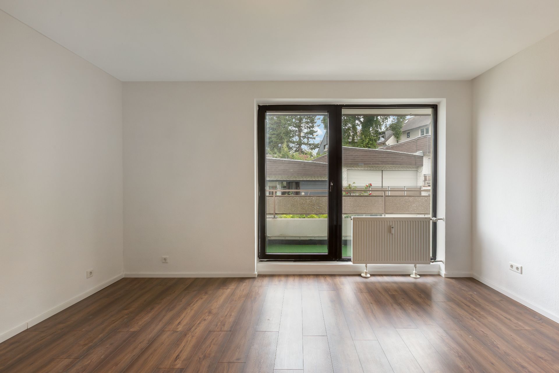 Leerer Raum mit Holzfußboden und großem Fenster mit Blick auf einen Balkon.