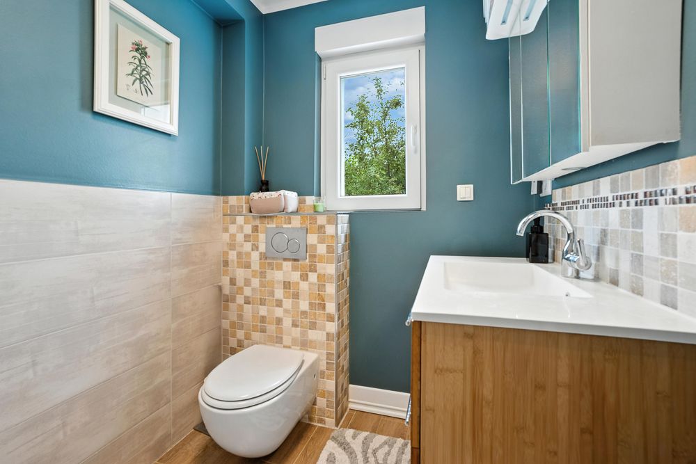 Modernes Badezimmer mit Wandtoilette, Waschbecken, Fenster und blauen Wänden.