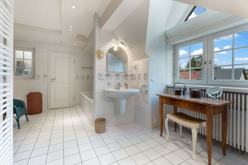 Helles Badezimmer mit Badewanne, Waschbecken, großem Fenster und Holztisch mit Hocker.