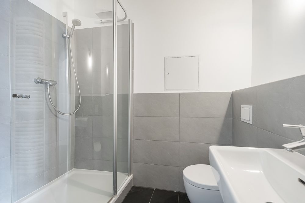 Modernes Badezimmer mit Dusche, WC und Waschbecken, graue Fliesen an den Wänden.