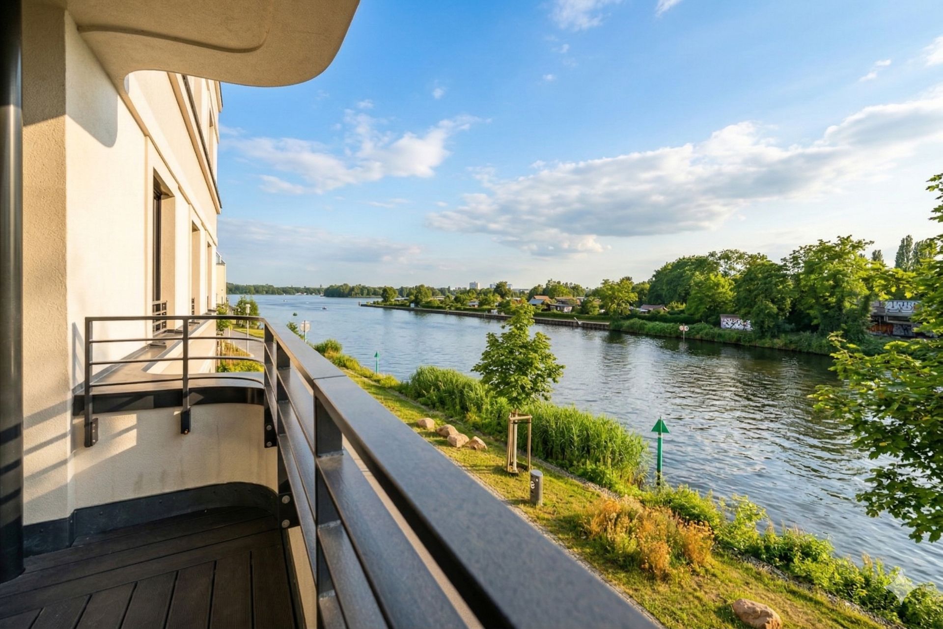 Balkon mit Blick auf einen ruhigen Fluss und grüne Uferlandschaft bei Sonnenschein.