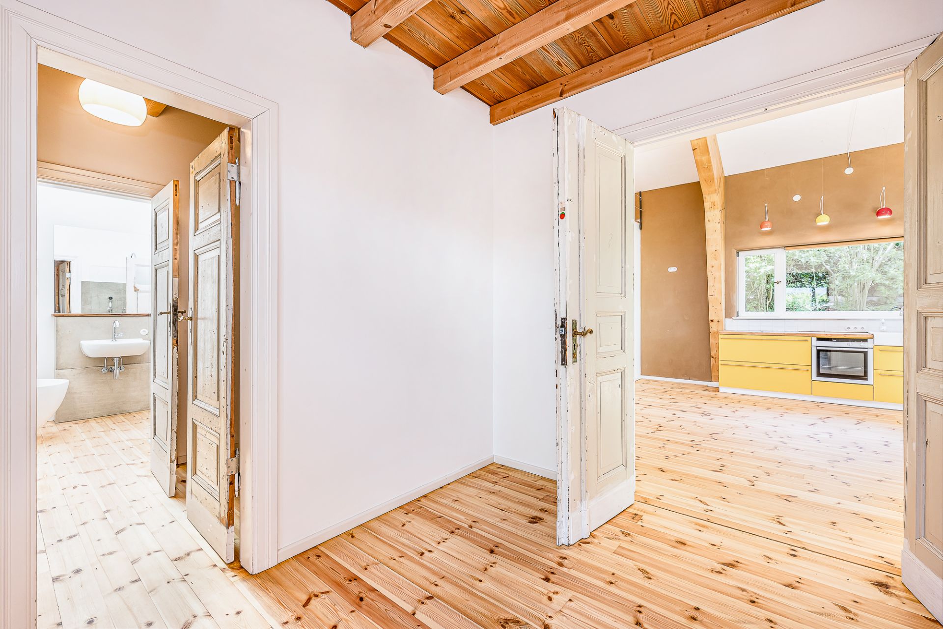 Heller Flur mit Holzboden, Zugang zu Bad und Küche mit gelben Schränken.
