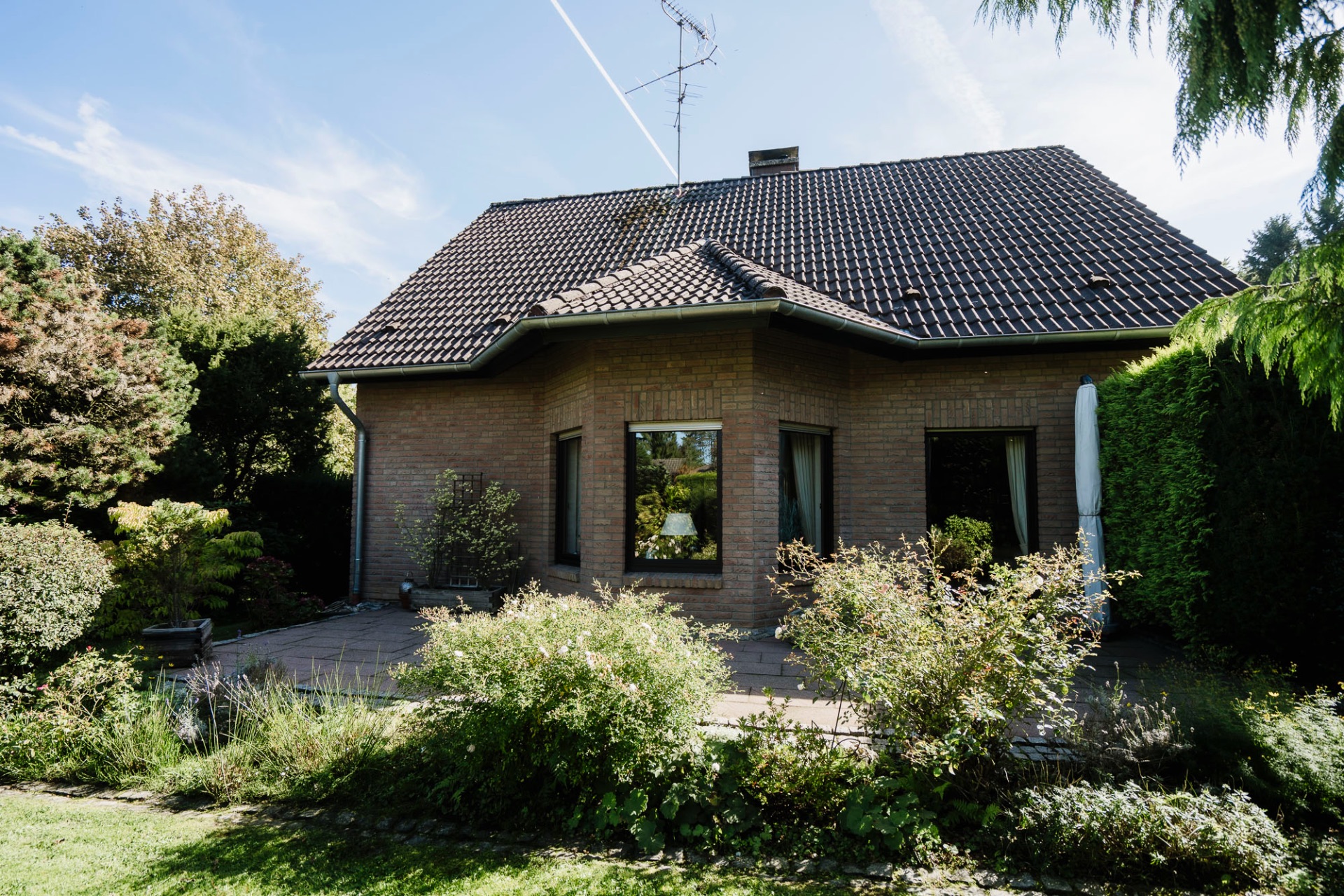 Einfamilienhaus mit großem Garten, Ziegelwänden und dunklem Dach bei sonnigem Wetter.