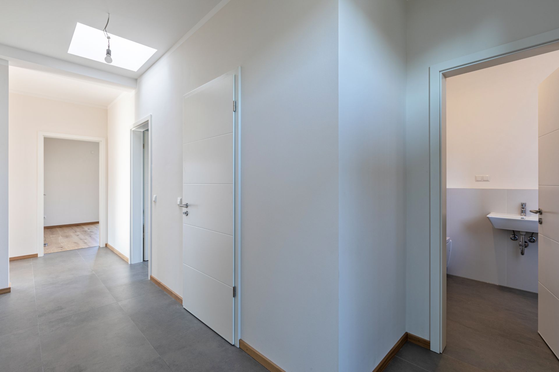 Heller Flur mit mehreren Türen, einer führt in ein Badezimmer mit Waschbecken.