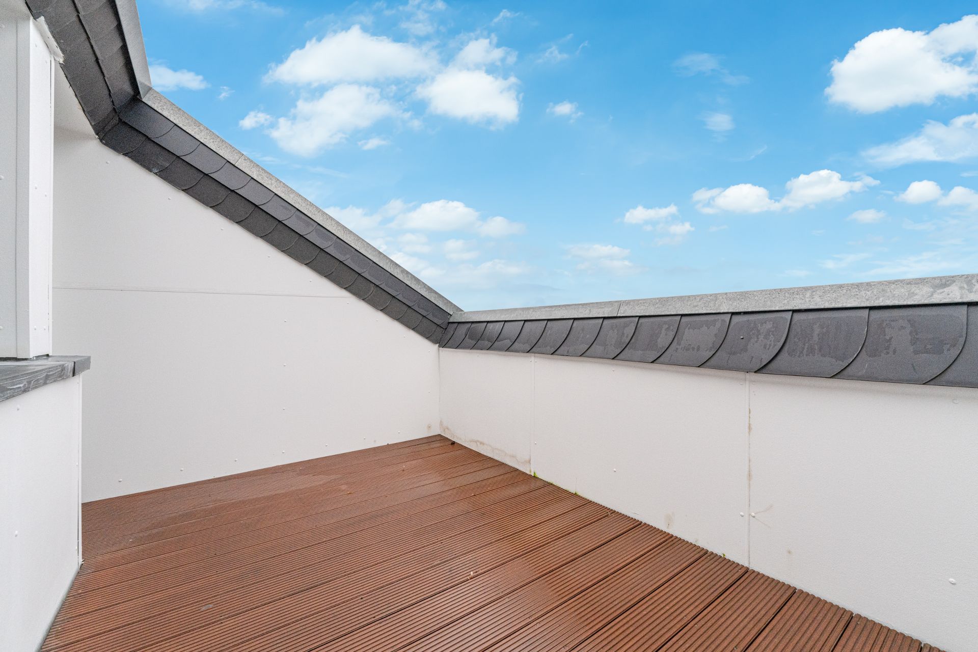 Kleine Dachterrasse mit Holzbelag und weißer Umrandung unter blauem Himmel.