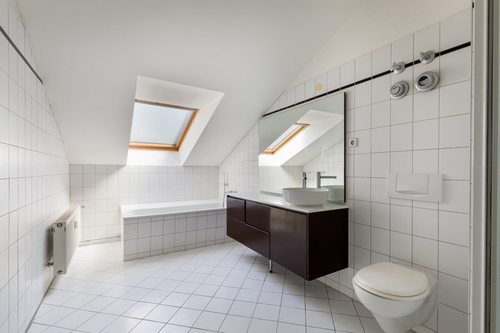 Modernes Badezimmer mit Dachfenster, Badewanne, großem Spiegel, Waschbecken und WC.