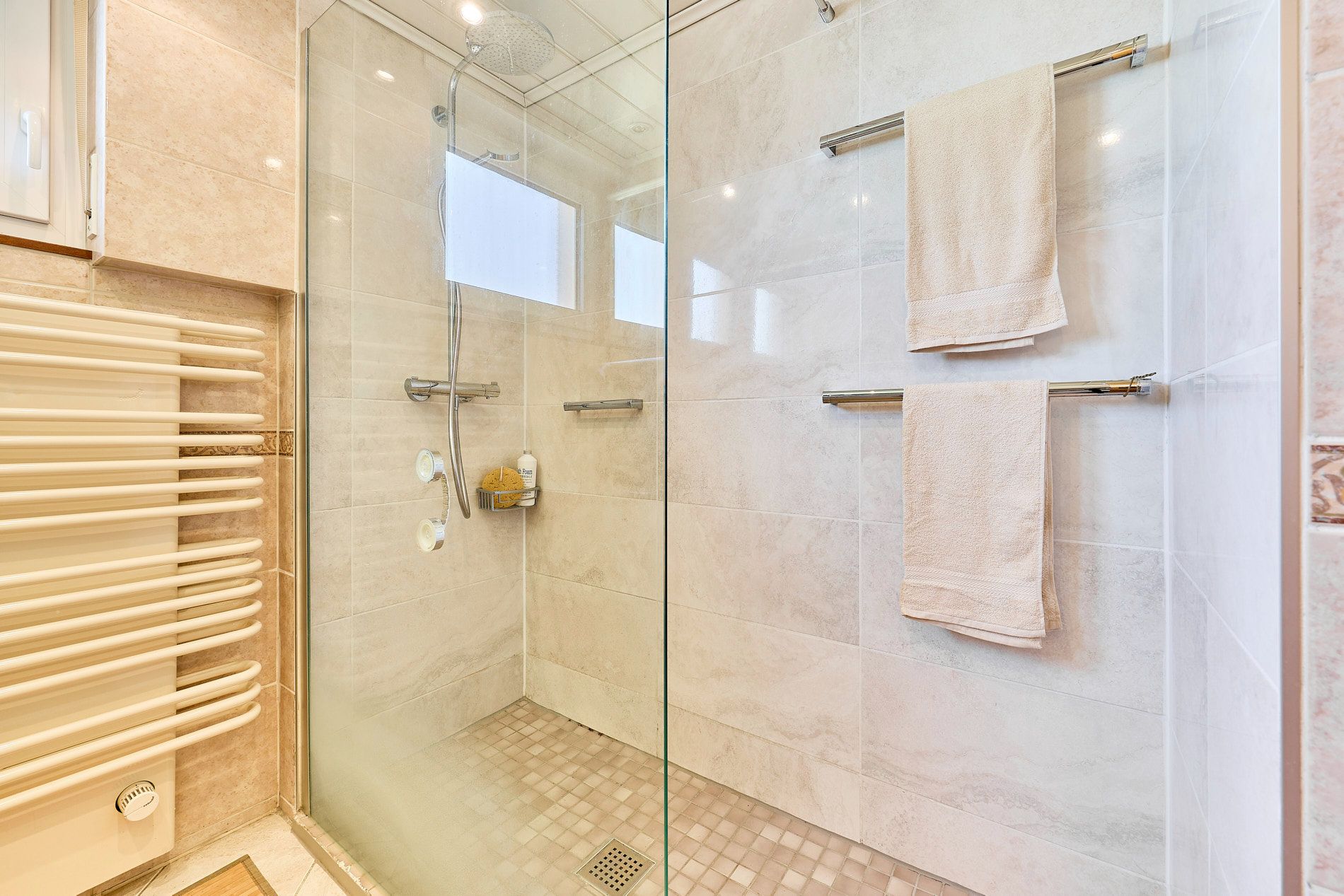 Helle, moderne Dusche mit Glaswand, Handtuchhaltern und Handtüchern an der Wand.