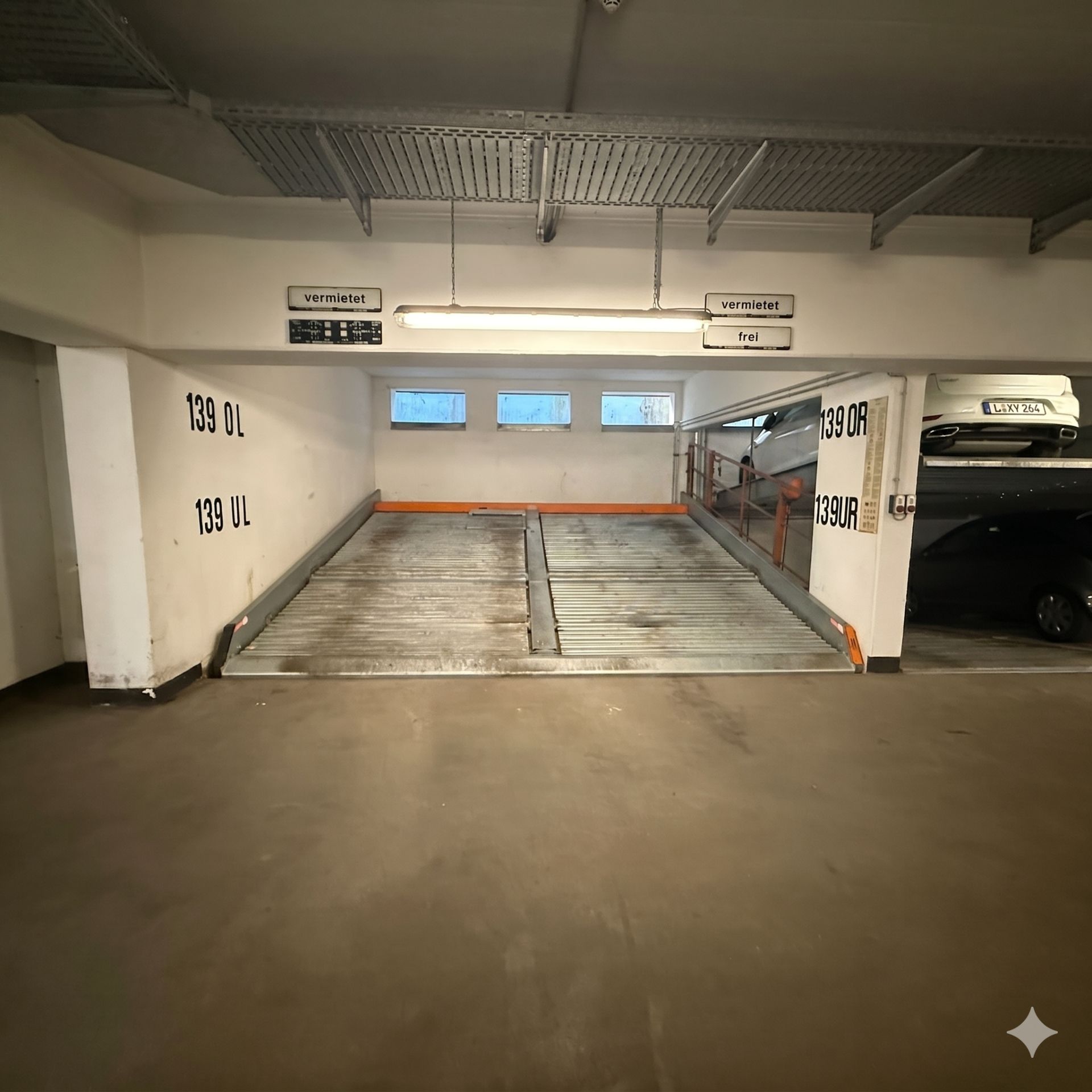 Parkplatz in einer Tiefgarage mit mechanischer Parkplattform und seitlichen Autoplätzen.