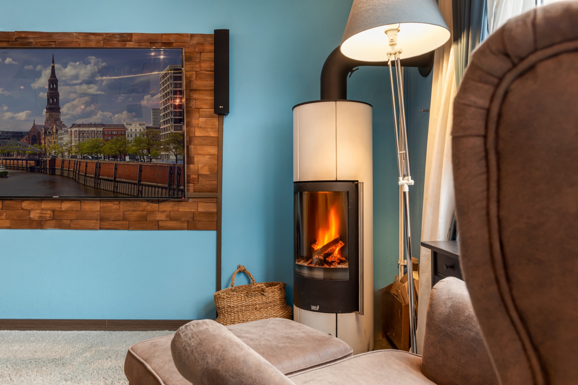 Gemütliches Wohnzimmer mit Sessel, Kamin, Stehlampe und Fernseher an blauer Wand.