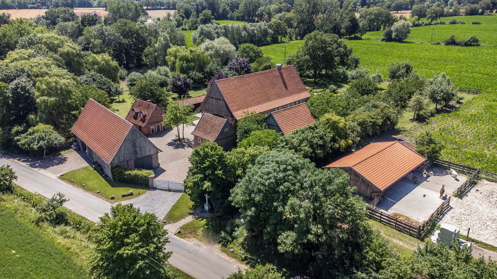 Luftaufnahme eines Bauernhofs mit mehreren Gebäuden und viel Grünfläche, umgeben von Feldern.