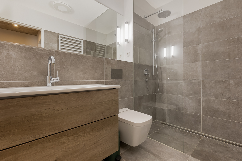 Modernes Badezimmer mit Holzwaschtisch, bodengleicher Dusche und grauen Fliesen.