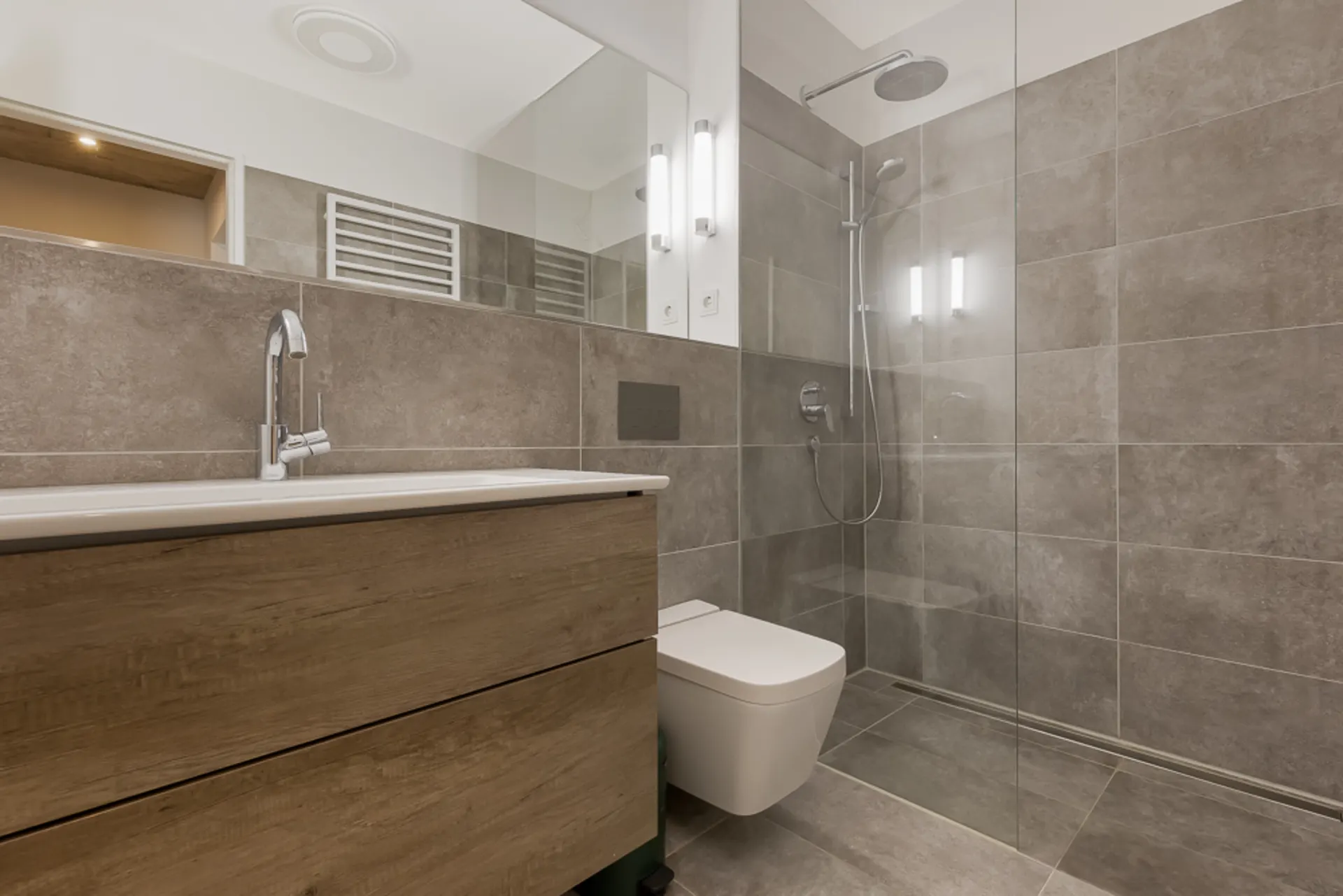 Modernes Badezimmer mit Holzwaschtisch, bodengleicher Dusche und grauen Fliesen.
