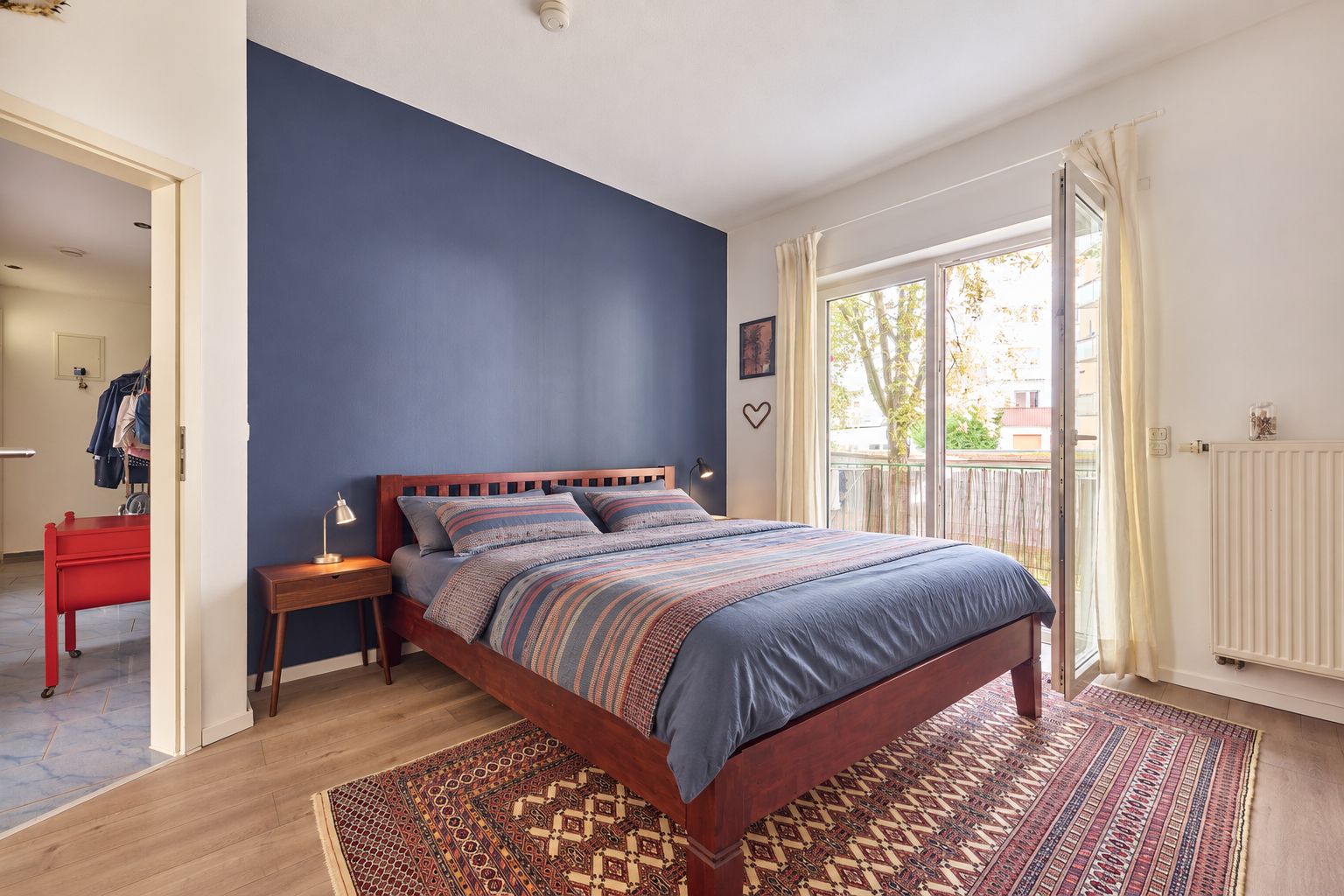 Schlafzimmer mit Doppelbett, dunkler Akzentwand, Teppich und offenem Zugang zum Balkon.