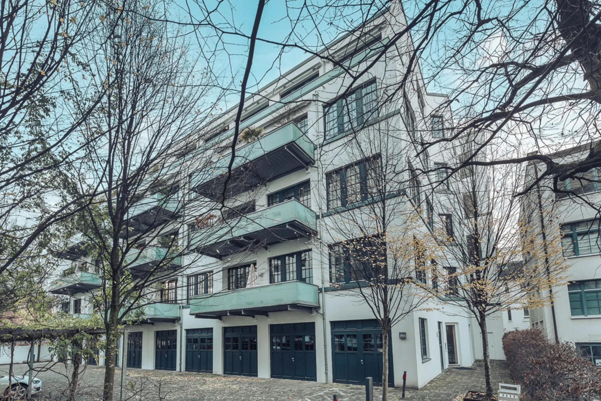 Mehrstöckiges Wohnhaus mit grünen Balkonen und großen Fenstern, umgeben von Bäumen.