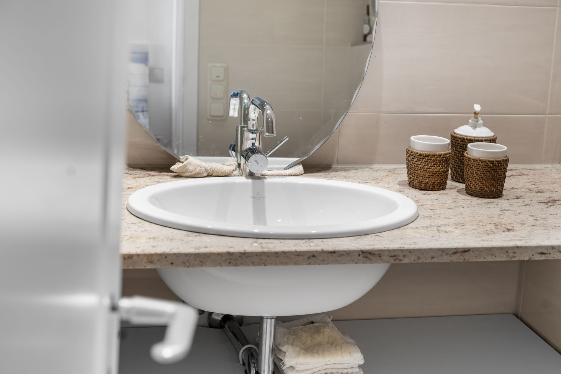 Waschbecken mit rundem Spiegel, Seifenspender und Bechern auf einer Marmorplatte im Badezimmer.