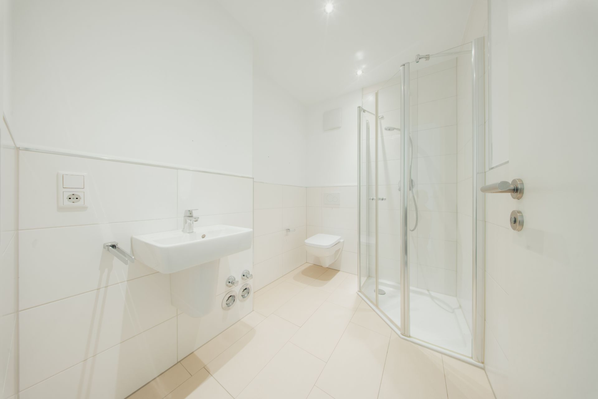Helles Badezimmer mit Waschbecken, wandhängender Toilette und Glasdusche.