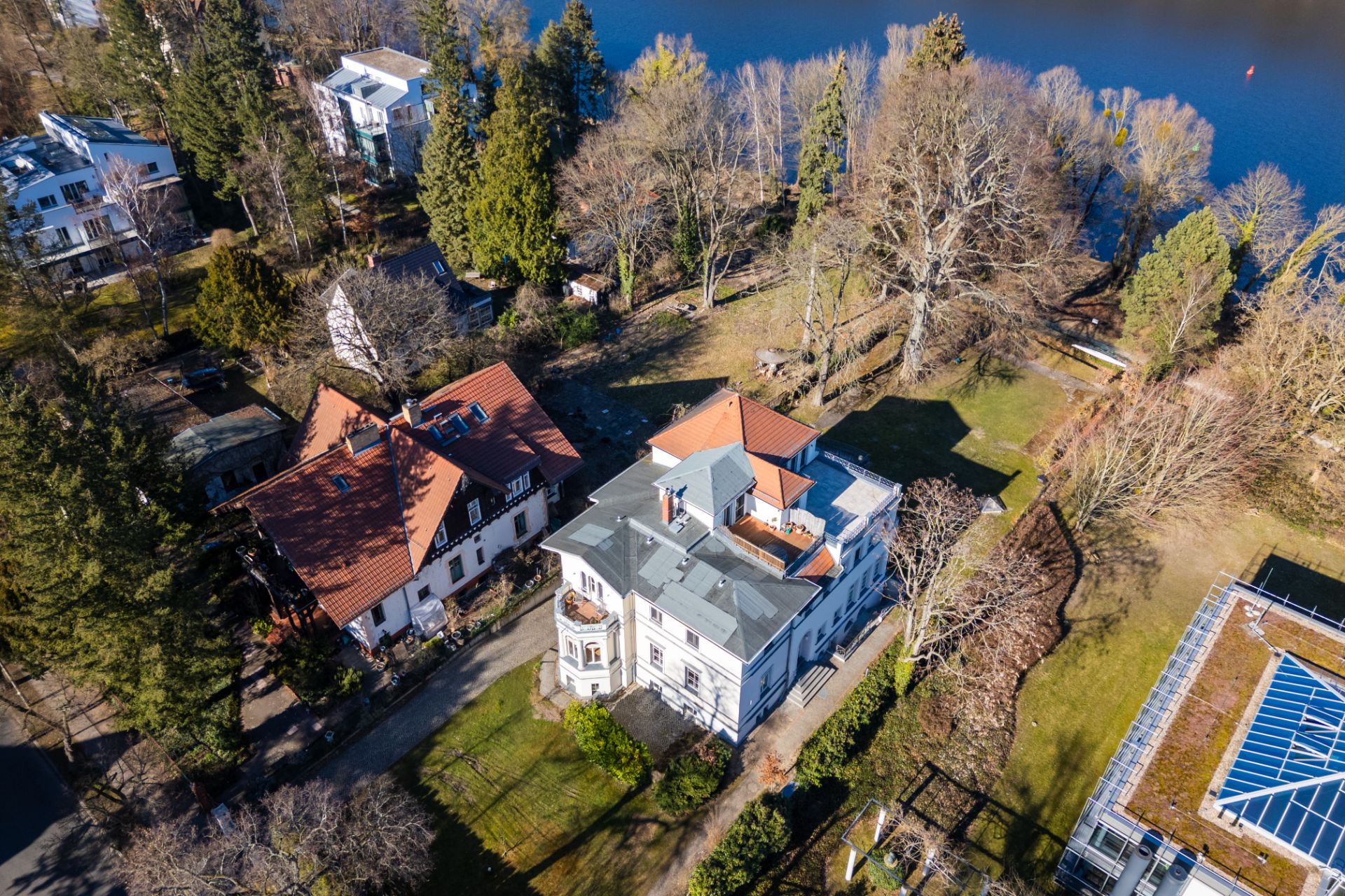Luftaufnahme eines großen Wohnhauses mit Garten und angrenzendem See im Hintergrund.