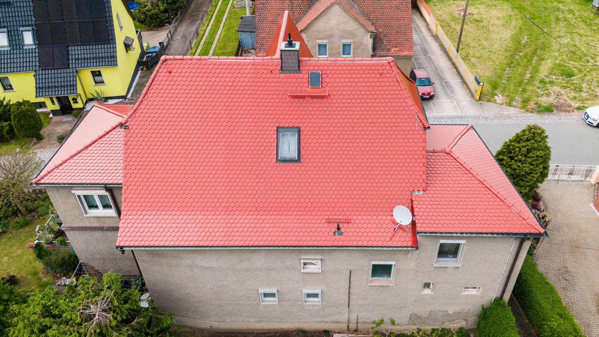 Haus mit rotem Ziegeldach und mehreren Fenstern, von oben aufgenommen.