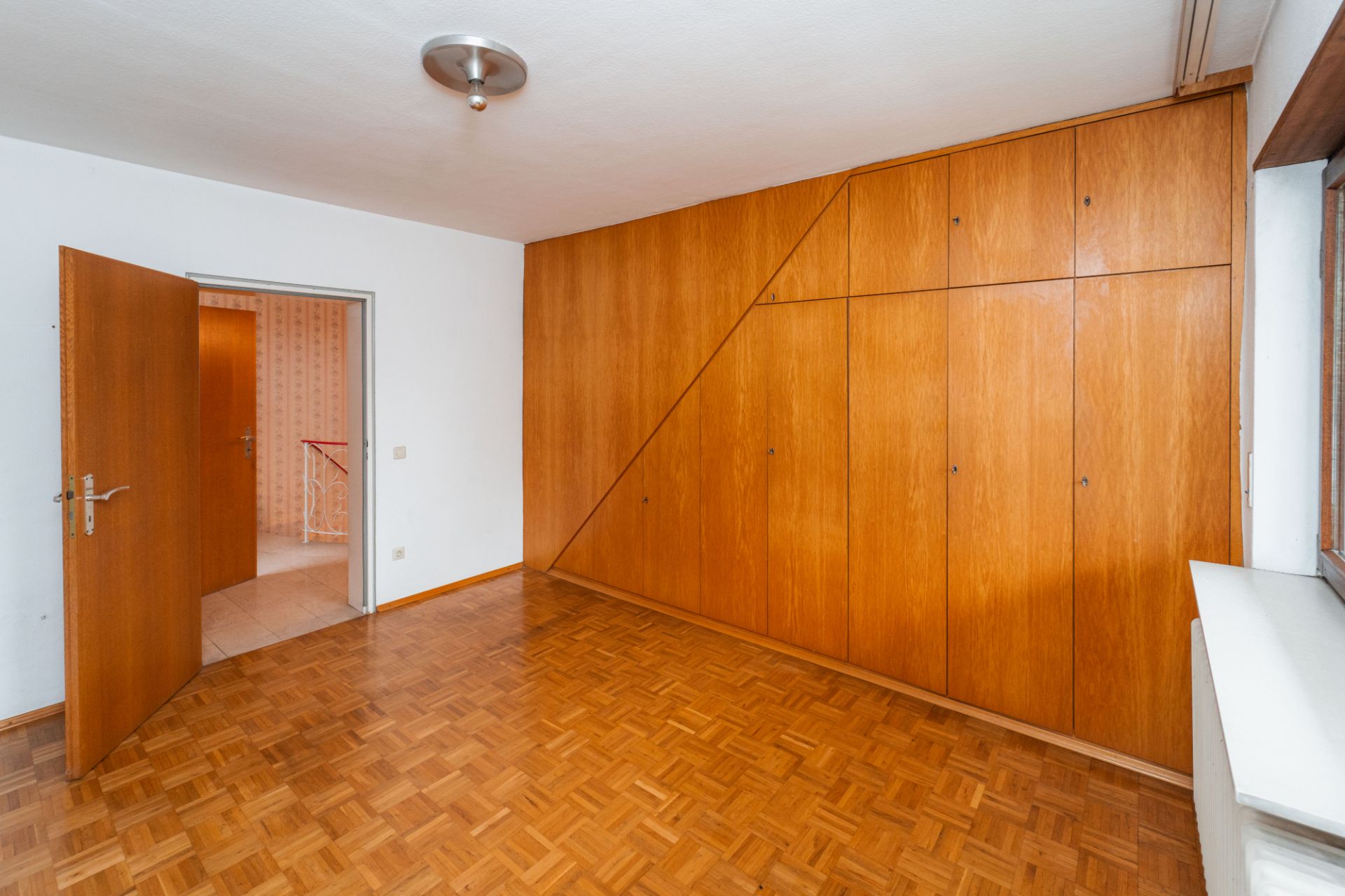 Zimmer mit Parkettboden, großem Holz-Einbauschrank und offen stehender Tür.
