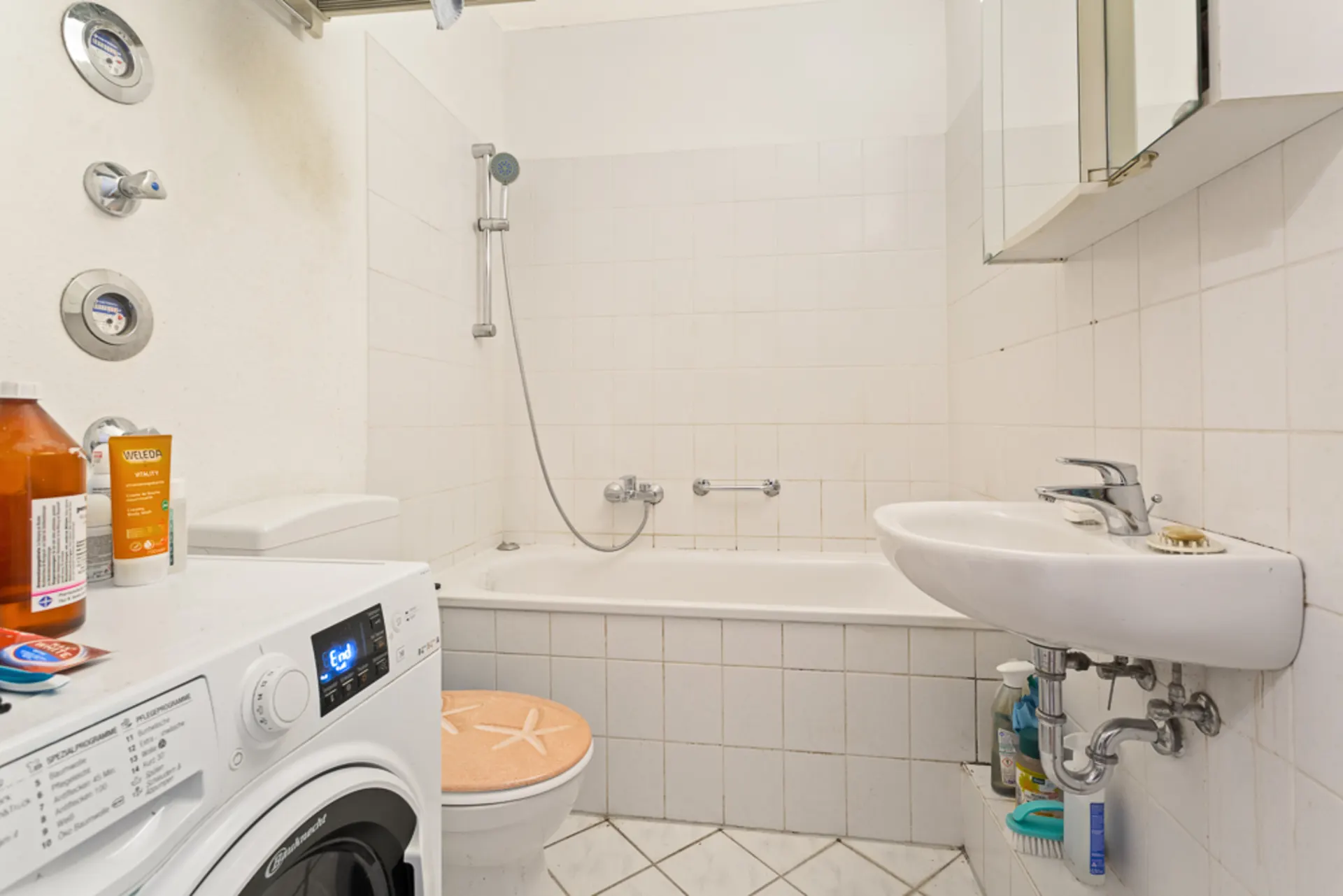 Kleines Badezimmer mit Badewanne, Waschmaschine, Waschbecken und Toilette.