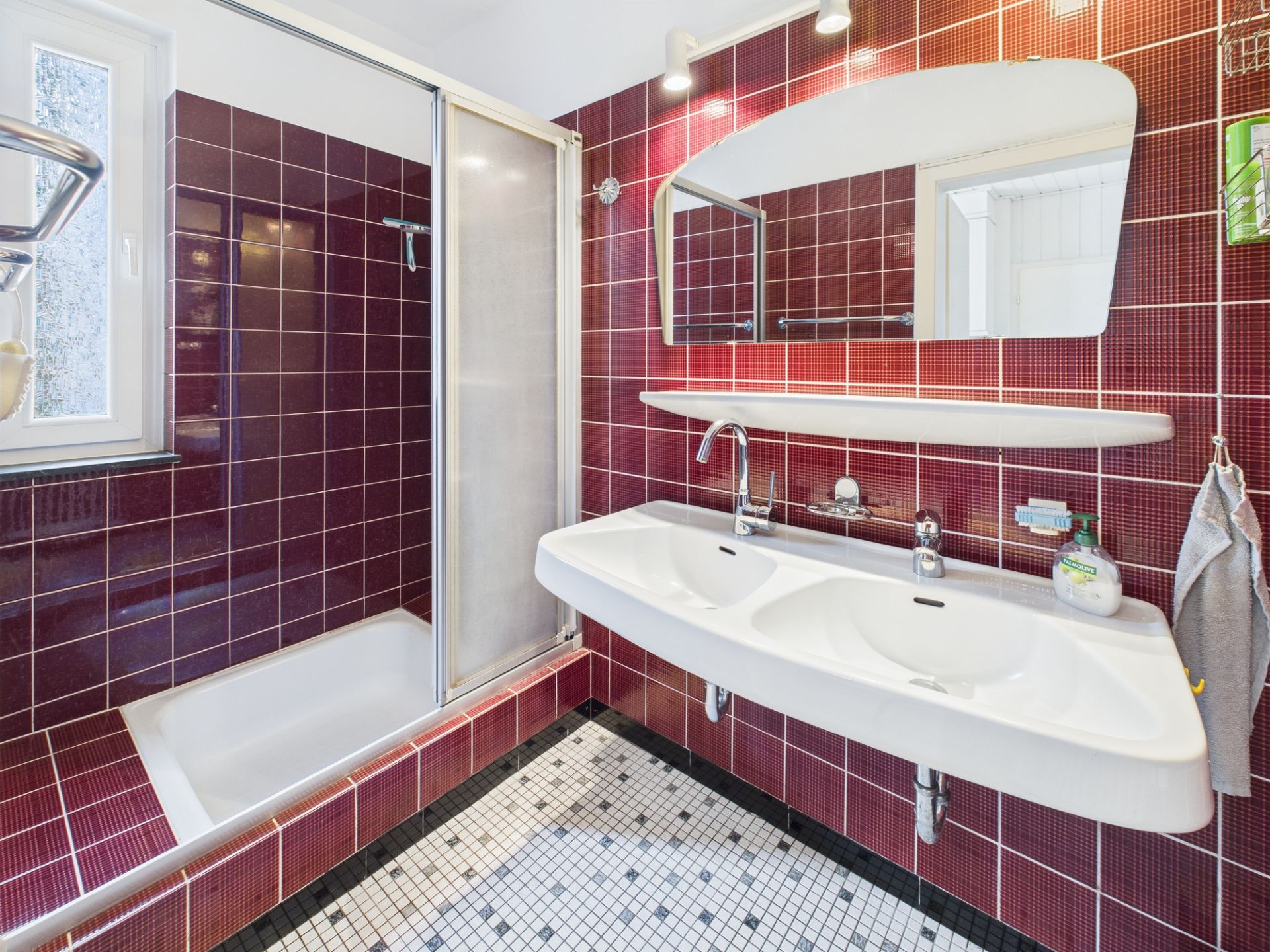 Badezimmer mit roten Fliesen, Doppelwaschbecken und Dusche mit Glastür.
