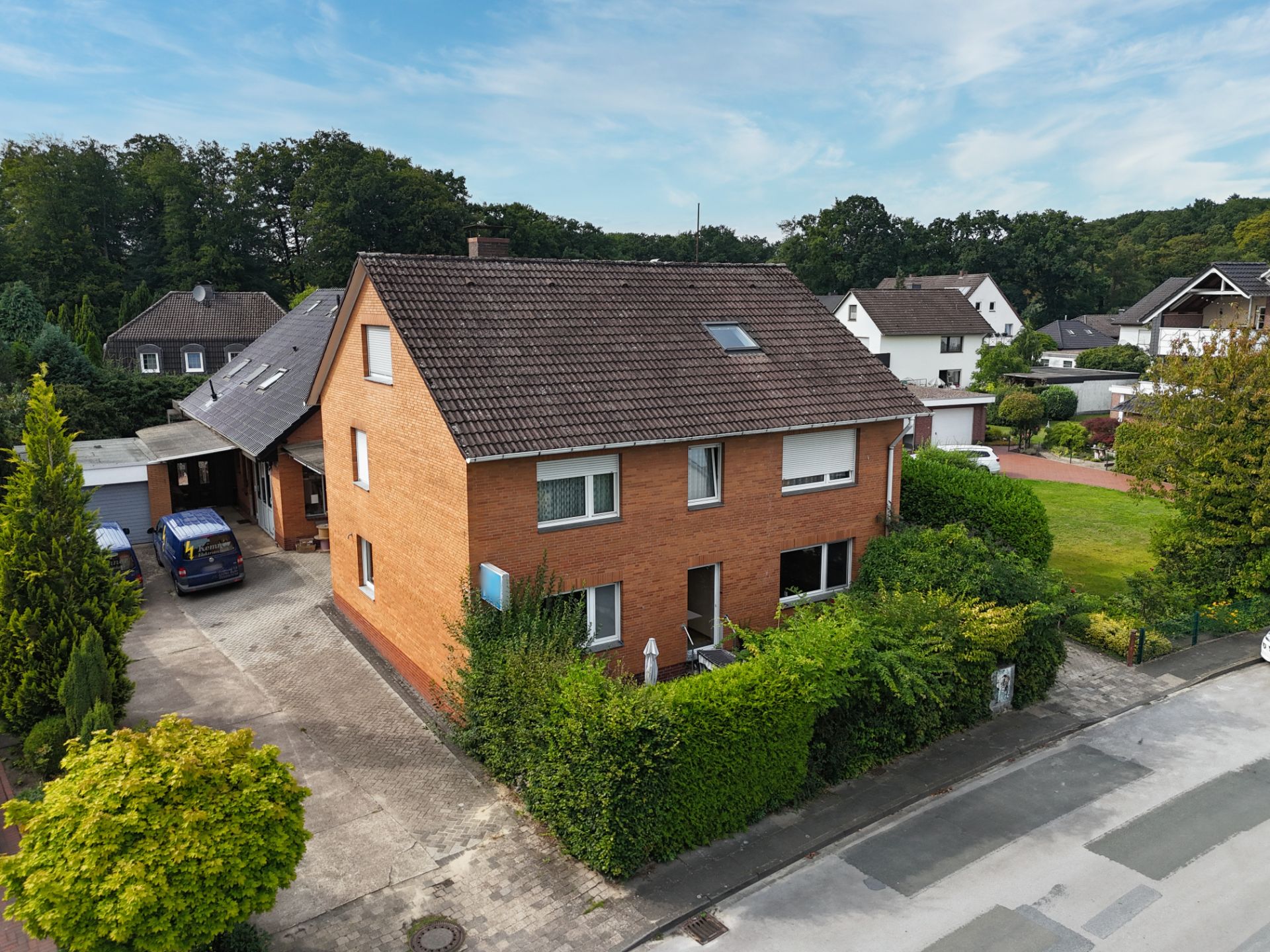 Zweistöckiges Backsteinhaus mit Dachfenster, Einfahrt und umgebenden Büschen in ruhiger Wohngegend.