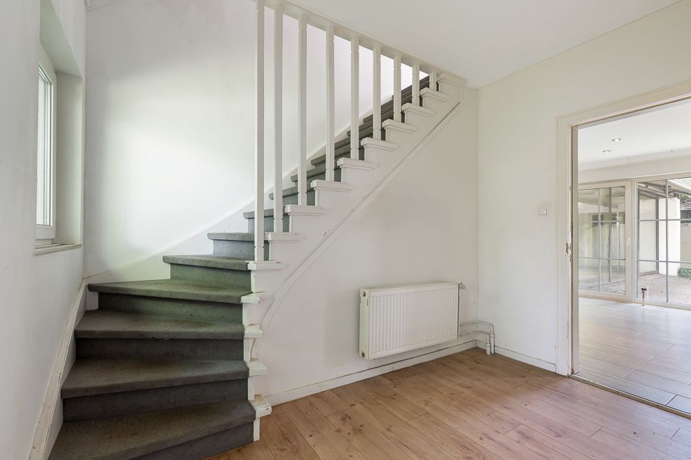 Heller Flur mit Holzfußboden, Treppe nach oben und Heizkörper an der Wand.