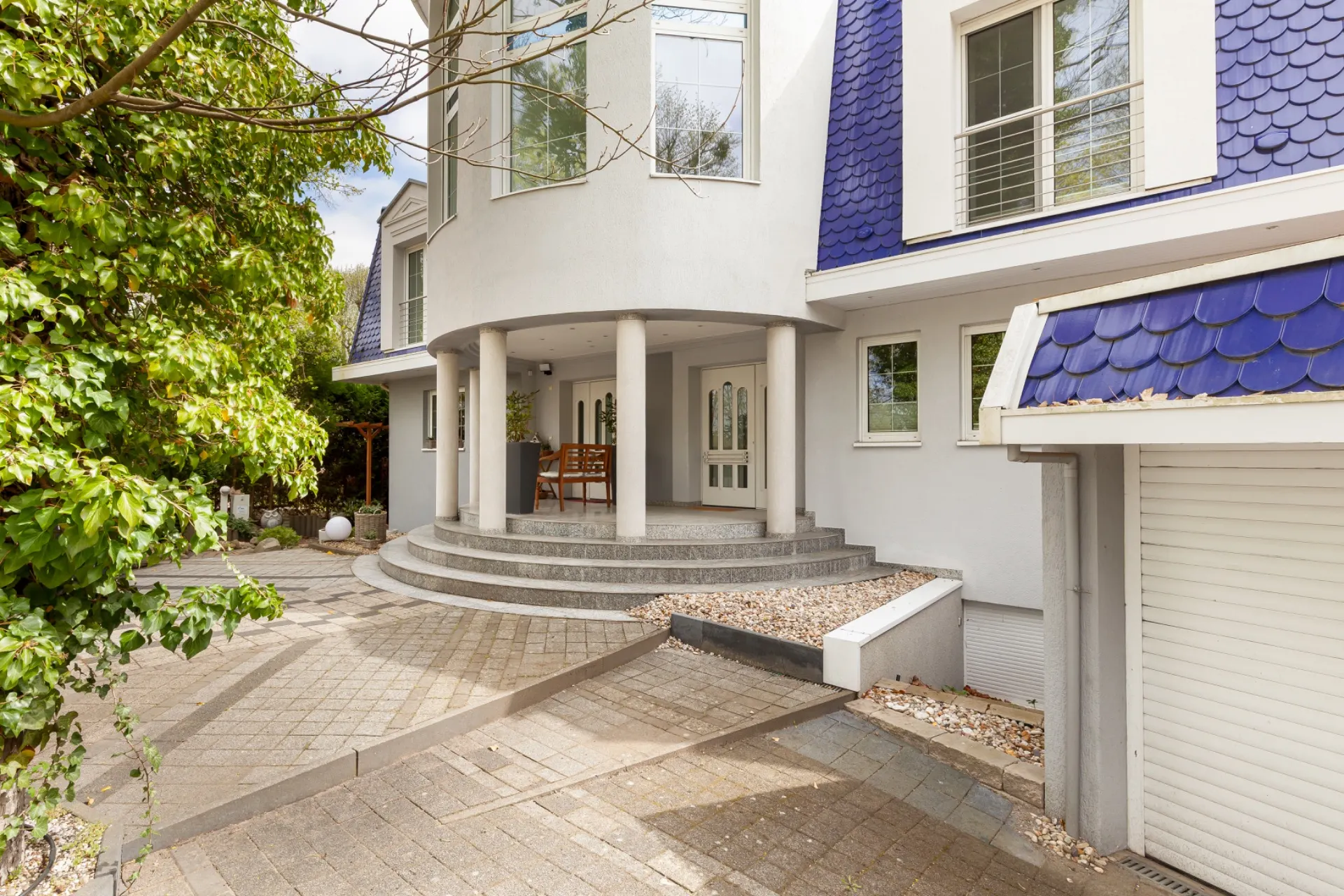 Eingang eines modernen Wohnhauses mit runden Säulen, blauen Dachziegeln und Garage.