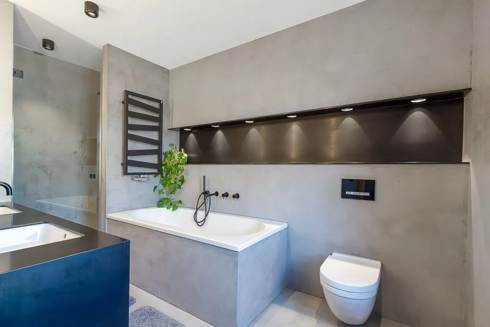 Modernes Badezimmer mit Badewanne, Waschbecken, Wandtoilette und beleuchtetem Regal.