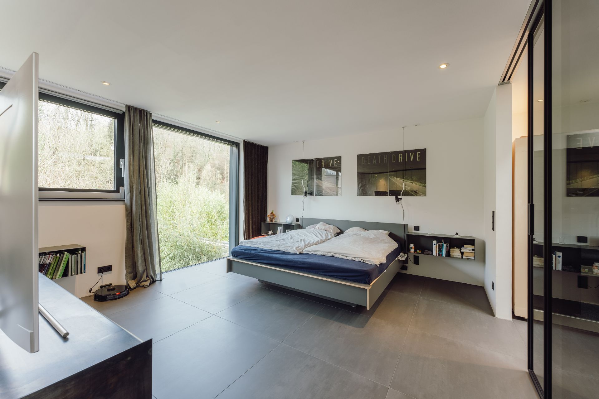 Modernes Schlafzimmer mit großem Bett, bodentiefen Fenstern und Bücherregalen an der Wand.