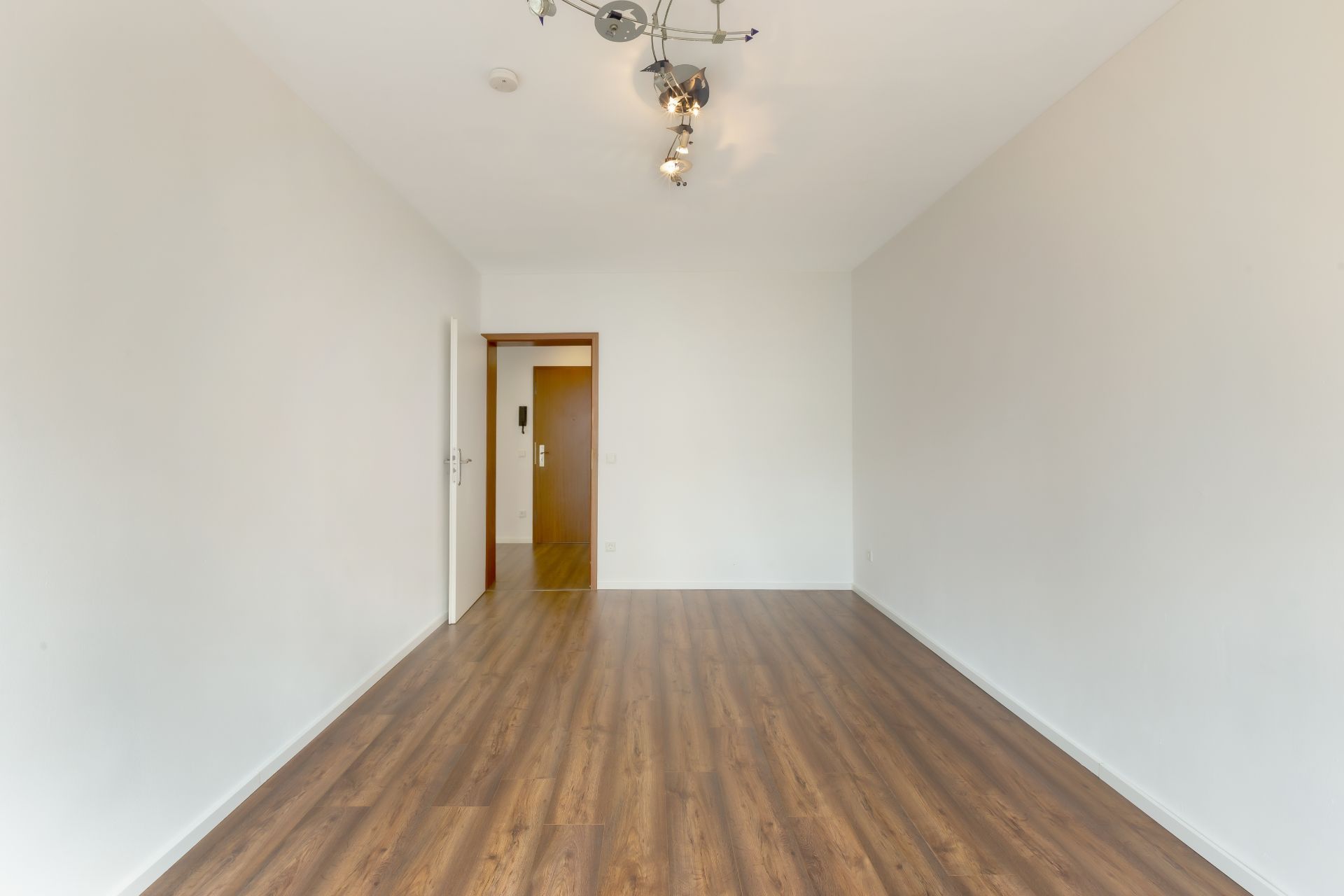 Leerer Raum mit Holzfußboden, weiß gestrichenen Wänden und Deckenleuchte.