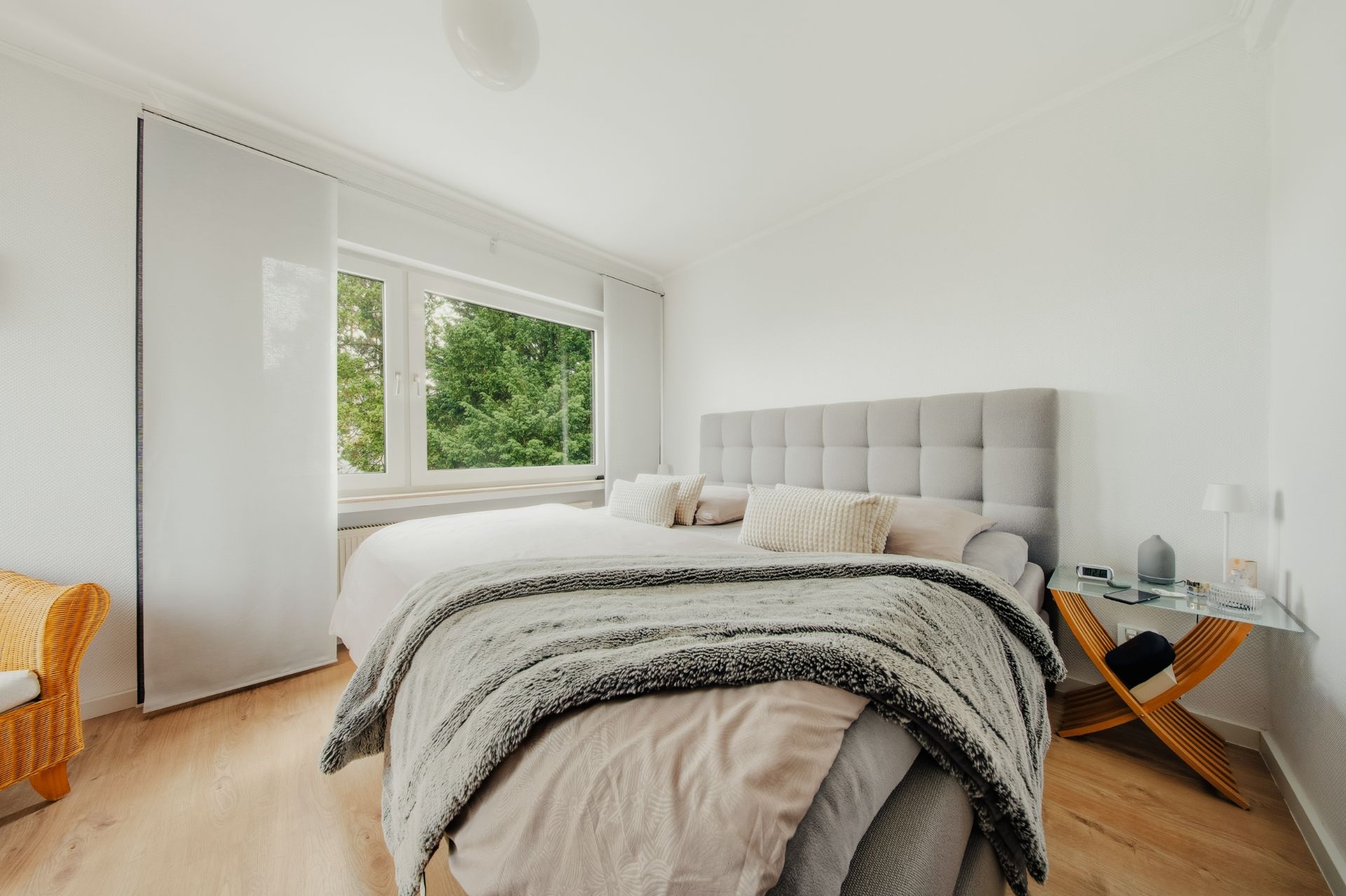 Helles Schlafzimmer mit großem Bett, Sessel und Fenster mit Blick ins Grüne.