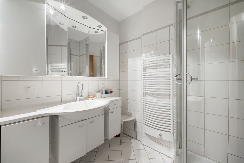 Modernes Badezimmer mit weißem Waschbecken, Spiegelschränken, Handtuchheizkörper und Dusche.